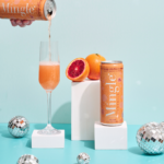 Pouring Mingle Mocktails Blood Orange into a flute glass, surrounded by fresh oranges and disco balls.