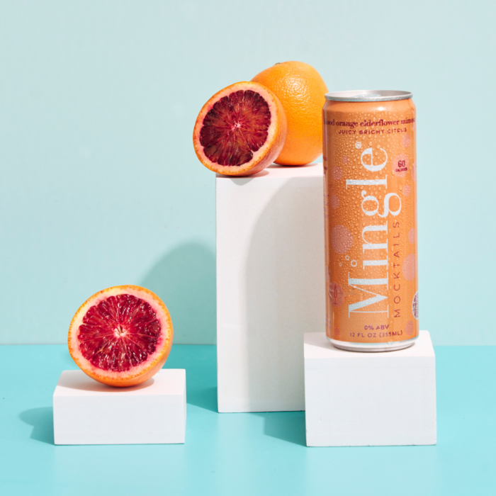 Mingle Mocktails Blood Orange can with fresh blood oranges on minimalist white blocks and blue backdrop.