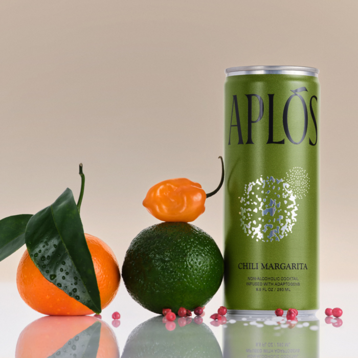 Green APLOS can with citrus fruits, habanero pepper, and pink peppercorns on a reflective surface.