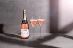 Rosé sparkling wine bottle with two filled glasses on a textured background, radiating elegance.