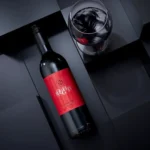 Luxurious red wine bottle with a matching glass on a sleek black geometric background.