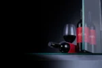 Red wine bottle with a filled glass on a reflective surface, set against a dark, minimalist background.