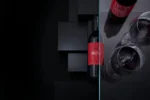 Stylish red wine bottle and glass on a reflective surface, paired with a modern black geometric backdrop.