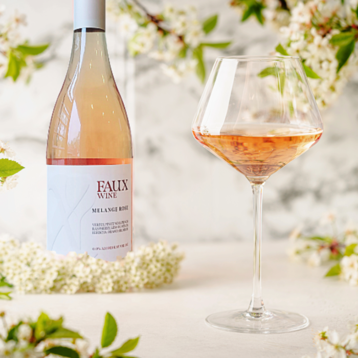 Faux Wine Melange Rosé bottle with a filled glass surrounded by blooming flowers on a bright table.