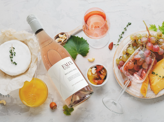 Melange Rosé wine bottle with gourmet cheese, fruits, nuts, and a filled glass on a marble table.