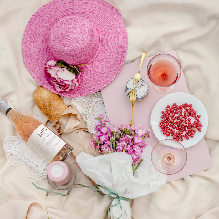 Faux Wine Melange Rosé bottle with pink hat, flowers, bread, berries, and elegant picnic setup.