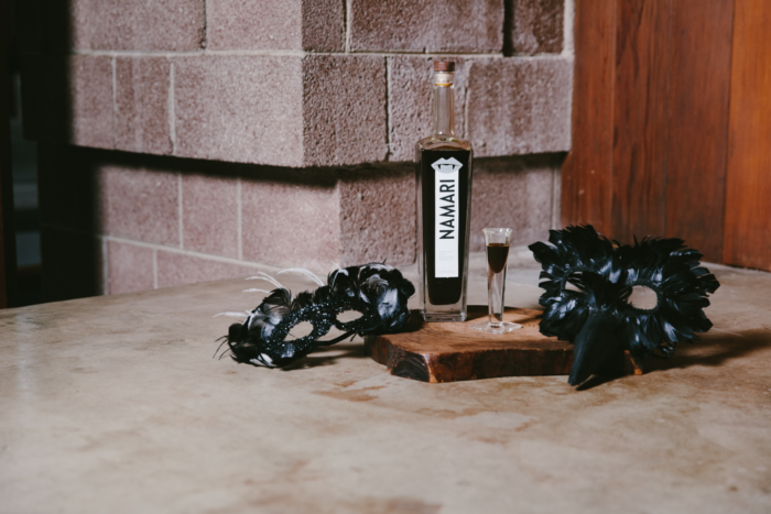 Memer non-alcoholic spirit bottle with a shot glass, black masquerade masks, and a rustic background.