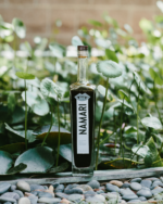 Namari non-alcoholic spirit bottle displayed among lush green foliage and natural stones.