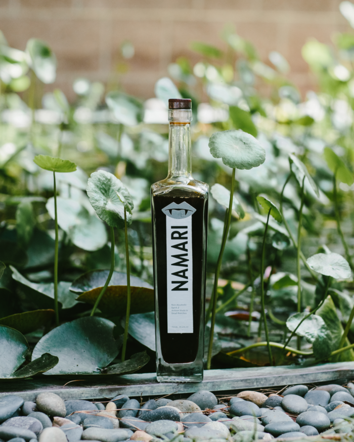Namari non-alcoholic spirit bottle displayed among lush green foliage and natural stones.
