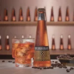Non-alcoholic cocktail bottle with a matching iced drink and coffee beans, set against a display of bottles.