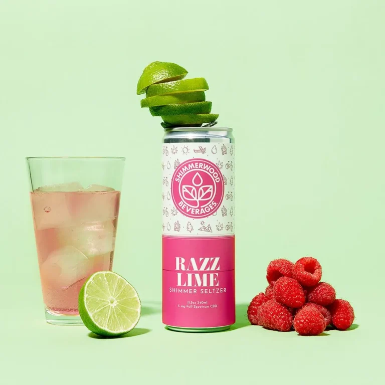 Shimmerwood Razz Lime seltzer can with stacked lime slices, a glass of pink drink, and fresh raspberries on a green background.