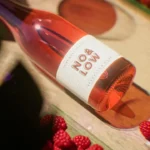 Close-up of No & Low rosé wine bottle with fresh raspberries on a sunlit table.