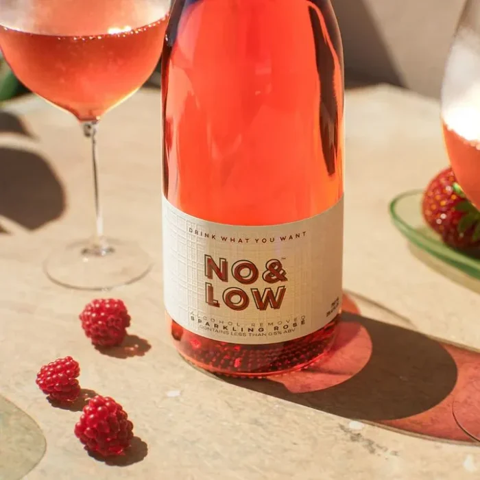 No & Low rosé wine bottle with fresh raspberries and glasses on a sunny tabletop.