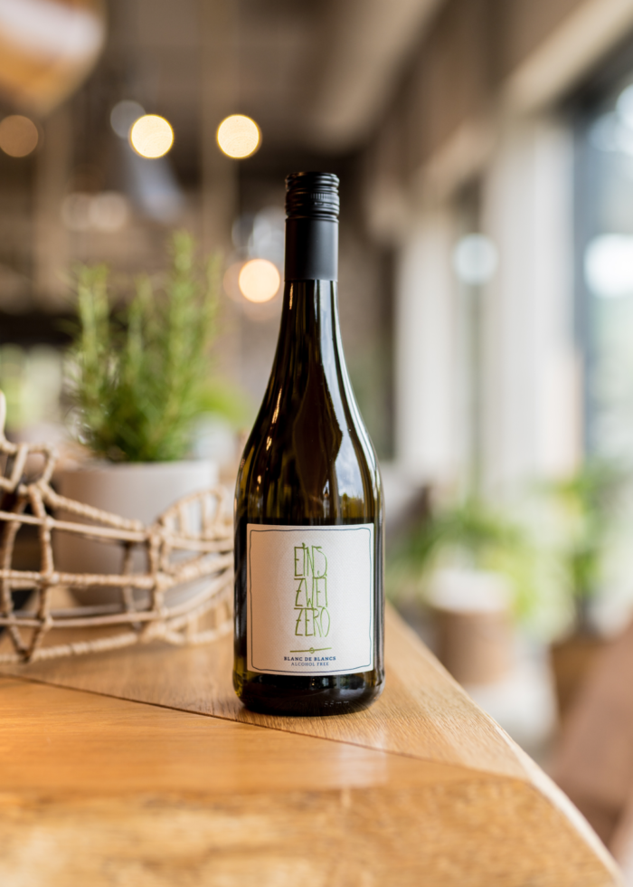 Bottle of white wine placed on a wooden table in a bright, modern setting with greenery in the background.