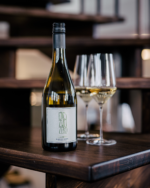 Bottle of white wine with two filled glasses on a wooden staircase in a sophisticated indoor setting.