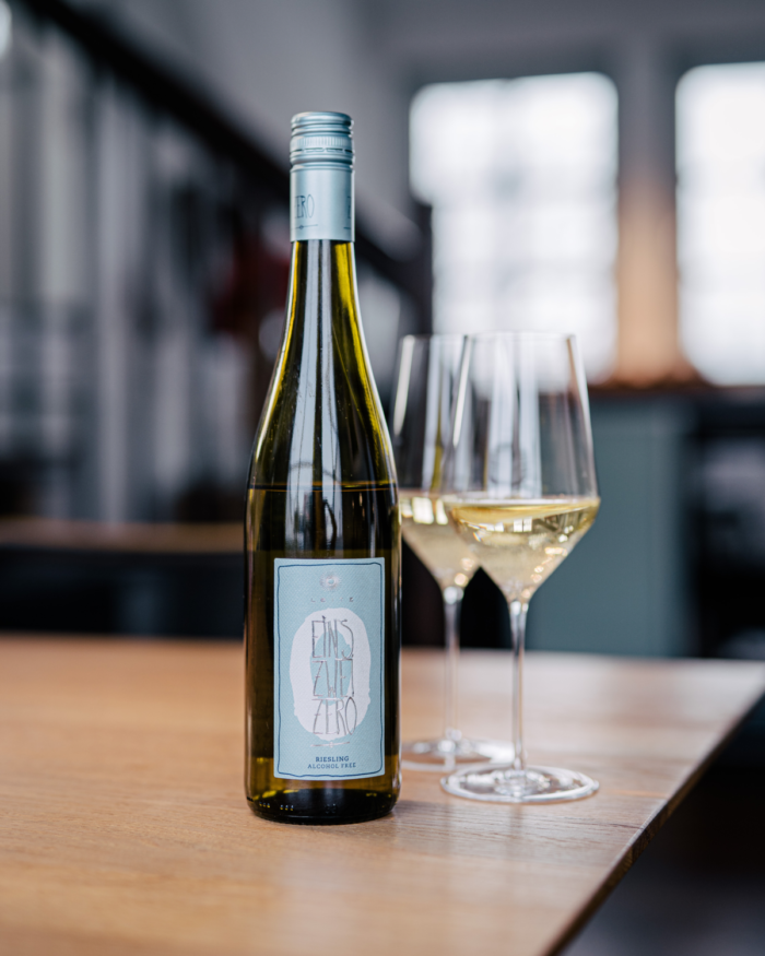 Bottle of white wine with two filled glasses on a wooden table in a modern, softly lit setting.