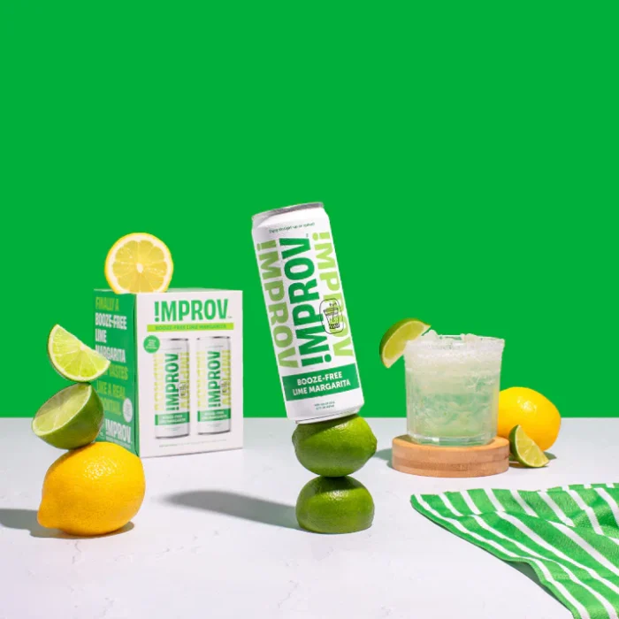 Improv Margarita drink can with limes, lemons, and a fresh cocktail against a vibrant green background.